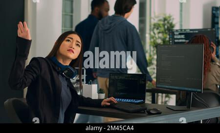 Asian coder turning head to work with holographic server code, typing html script on terminal window. Software engineer working with hologram of app database, writing system algorithm. Stock Photo