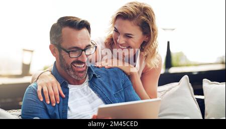 Taking a look at all our funny moments on holiday. an affectionate mature couple using a digital tablet while relaxing on a couch together outdoors. Stock Photo