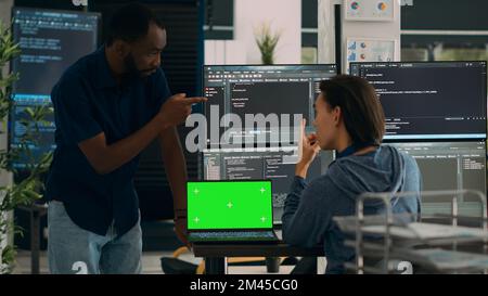 Diverse app developers working with greenscreen on laptop and programming source code with html script on monitor. Looking at isolated mockup template with chromakey display, copyspace. Stock Photo