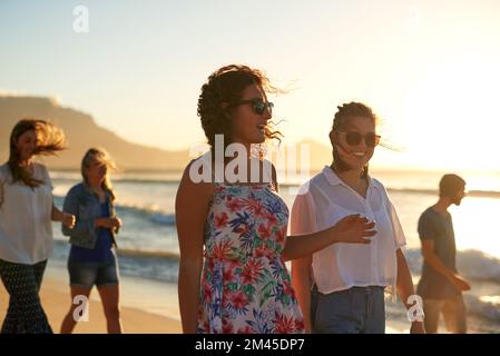 Summer, the beach and your bestie. two attractive young girlfriends having a chat while taking a walk on the beach with their friends. Stock Photo