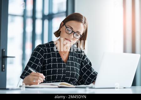 Embracing her work responsibilities. a focused young businesswoman writing on a notebook in an office. Stock Photo