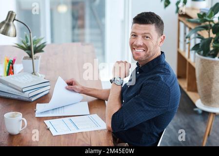 Hes having a great day at the office. a handsome mature businessman looking through some paperwork while sitting in his office. Stock Photo