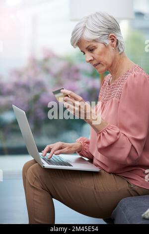 Time to do a little shopping online. a mature woman using her laptop while holding her credit card at home. Stock Photo