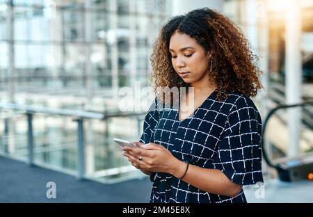 Let me update the team on the new agenda. an attractive young businesswoman using a smartphone in a modern office. Stock Photo
