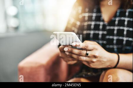 Smart businesswomen opt for smart devices. an unrecognizable businesswoman using a smartphone while sitting on a couch in a modern office. Stock Photo