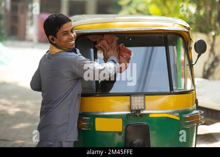 Young man cleaning front glass of his auto rickshaw Stock Photo