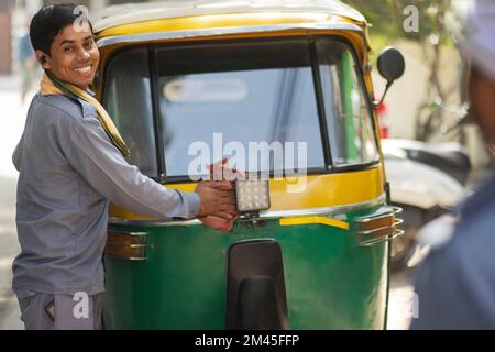 Young man cleaning front glass of his auto rickshaw Stock Photo