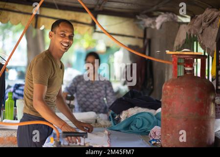 Smiling Man, dhobi ironing clothing outside using a gas cylinder Stock Photo