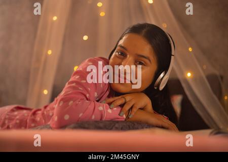 Portrait of a teenage girl listening music on headphones while lying on bed Stock Photo
