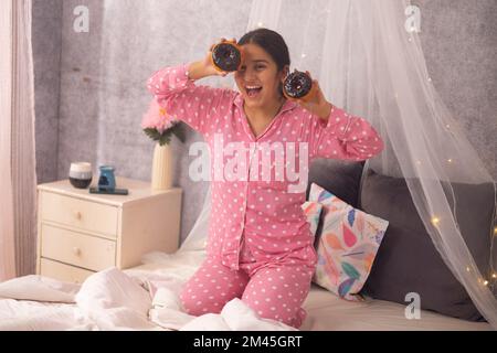 Portrait of a teenage girl holding doughnuts in her hands while kneeling on bed Stock Photo