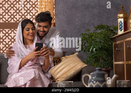 Happy Muslim couple using mobile together in living room Stock Photo