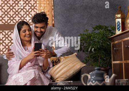 Happy Muslim couple using mobile together in living room Stock Photo