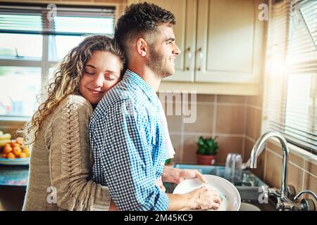 I love you for all you are. a young woman embracing her boyfriend from behind while he does the dishes. Stock Photo