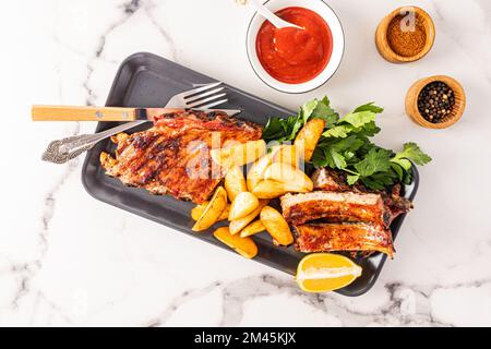 Top view of the ceramic dark tray with pork ribs grill and grilled potatoes with spices and herbs. marble white background. culinary menu Stock Photo