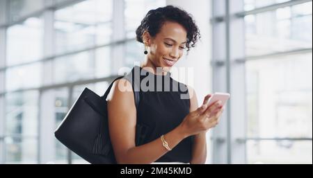 Shes constantly looking for new connections. a young businesswoman using a smartphone and waving while walking through a modern office. Stock Photo