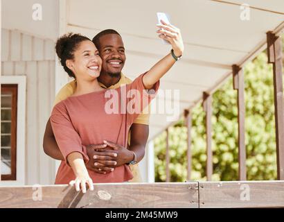 Love, phone selfie and black couple in home by balcony, bonding and having fun. Romance, hug and man and woman taking pictures on mobile smartphone Stock Photo