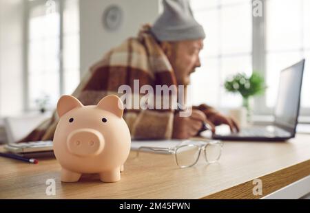 Close up of piggy bank on table with senior retired man using laptop computer in background Stock Photo