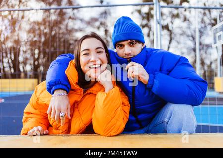 Multiracial young couple of lovers dating outdoors in winter, wearing winter jackets and having fun - Multiethnic millennials bonding in a urban area, Stock Photo