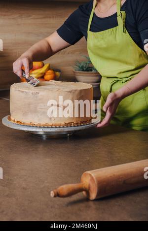 Unrecognisable woman decorating a delicious layered sponge cake with chocolate icing cream. DIY, sequence, step by step, part of series. Stock Photo