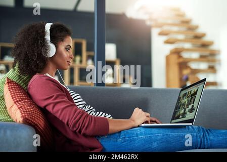 Weekends are for doing what relaxes you. a young woman using headphones and a laptop on the sofa at home. Stock Photo
