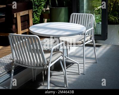 Outdoor small table set at the restaurant or cafe. Two empty chairs with pads and empty white round table in front of the coffee shop. Stock Photo