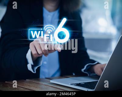 Wi-Fi 6 speed logo glowing on virtual screen while businesswoman pointing hand and using laptop computer. Wifi6 technology new generation telecommunic Stock Photo