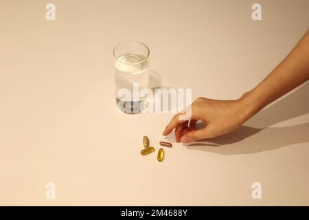 Woman is taking medicine with cup of water on the white table, girl is taking nutritional supplement by hand Stock Photo