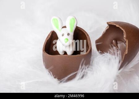 White Easter Bunny in a cracked chocolate egg iand empty egg shell in nest of white feathers. Easter marzipan rabbit in a cracked chocolate egg. Sweet Stock Photo