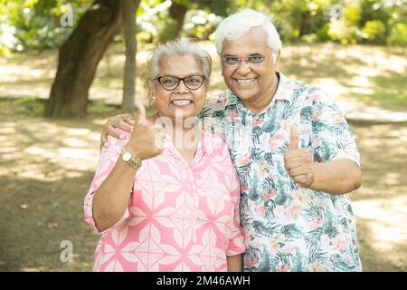 Happy indian senior couple give thumbs up pose at summer park. Old people enjoying life. Stock Photo