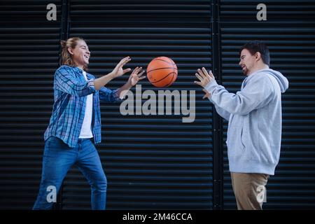 Man with down syndrome playing basketball outdoor with his friend. Concept of friendship and integration people with disability into society. Stock Photo