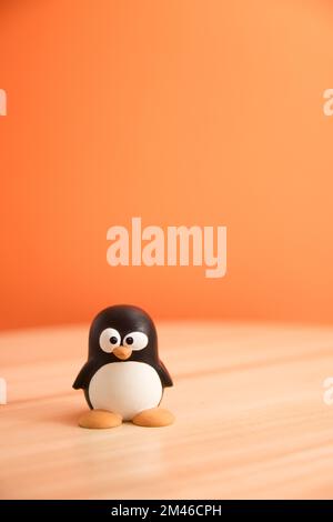 Image of Tux, the penguin that is the emblem of the GNU/Linux operating system. In the image it appears isolated on a table with copy space and orange Stock Photo