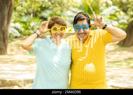 Portrait of crazy excited funny senior indian couple wearing funky eye glasses outdoor at park. Mature people making faces. Stock Photo