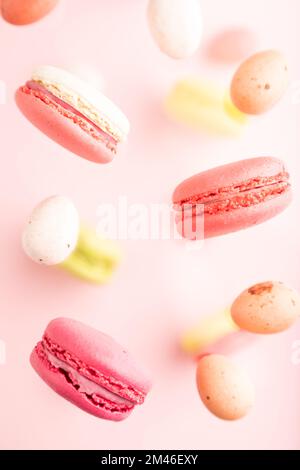Multicolored flying macaroons and chocolate eggs frozen in the air on blurred pink background. top view, flat lay, close up. Breakfast, morning, conce Stock Photo