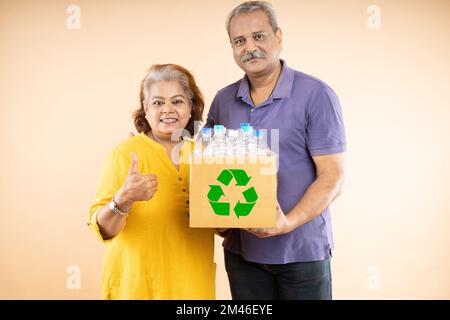 Happy eco-friendly indian senior couple holding a box full of plastic bottles for recycling. Environmental protection, Earth day concept Stock Photo