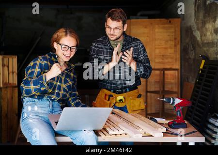 Woman and man celebrating teamwork success of their small business while working in their carpentry workshop. Stock Photo