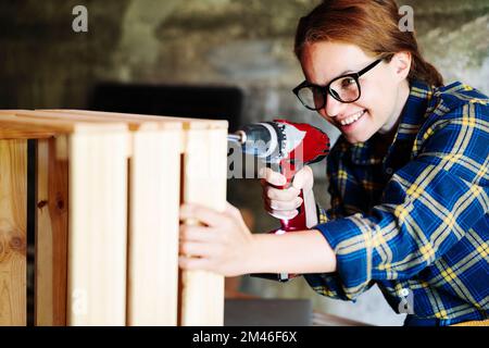 Woman in glasses using drill in workshop. Stock Photo
