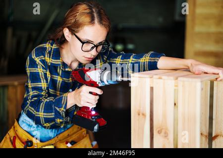 Woman in glasses using drill in workshop. Stock Photo