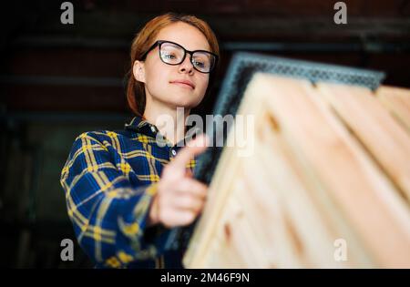 Young woman wearing glasses measuring wooden object using angle rulet. Stock Photo