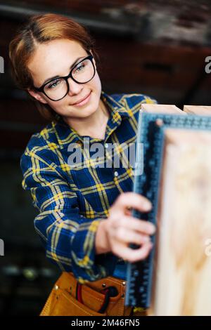 Young woman wearing glasses measuring wooden object using angle rulet. Stock Photo