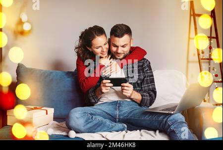 Happy young married couple together using their smart phone while at home enjoying christmas holiday. Stock Photo