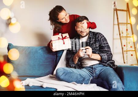 Young family at home while christmas holiday woman giving christmas gift while man using his mobile phone. Stock Photo
