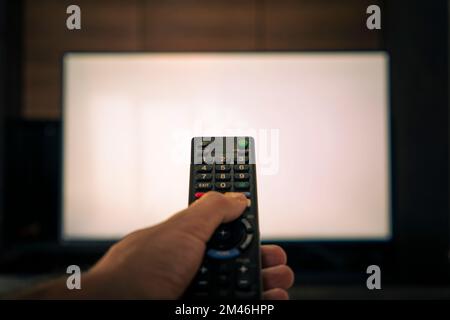 blurred remote control for television. a man's hand holds the remote control in front of a large white TV screen. Stock Photo