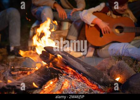 Unrecognizable friends having fun playing music and enjoying bonfire camping in nature at night Stock Photo