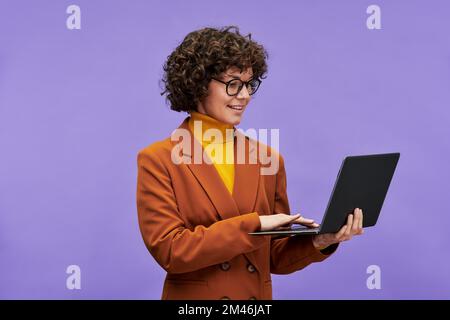 Young confident brunette female teacher or chief executive officer in formalwear holding laptop and looking at screen during network Stock Photo