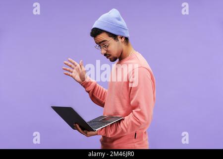 SIde view of young astonished male programmer in casualwear and eyeglasses looking at laptop screen while facing technical problem Stock Photo