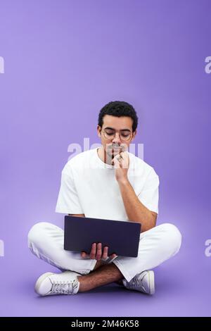 Young serious man with laptop on his knees watching online video or working over new business project while sitting in front of camera Stock Photo
