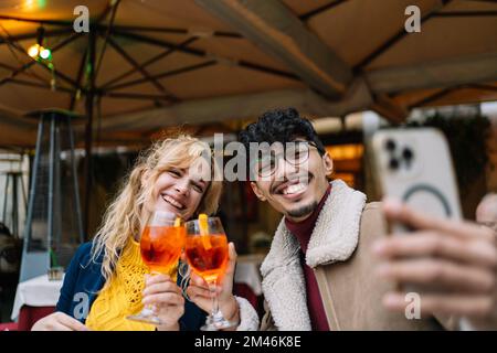 Young multi-ethnic smiling couple taking a selfie while sitting in a restaurant having a drink Stock Photo