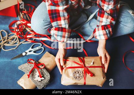 High angle view of female hands and Christmas gift in brown craft paper and red ribbon. Stock Photo