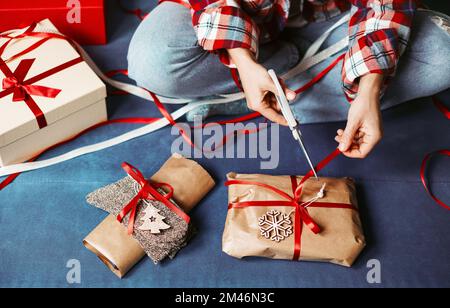 Packing Christmas gifts using brown craft paper and cutting red ribbon. Stock Photo