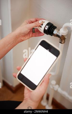 Woman holding phone and using radiator thermostat Stock Photo